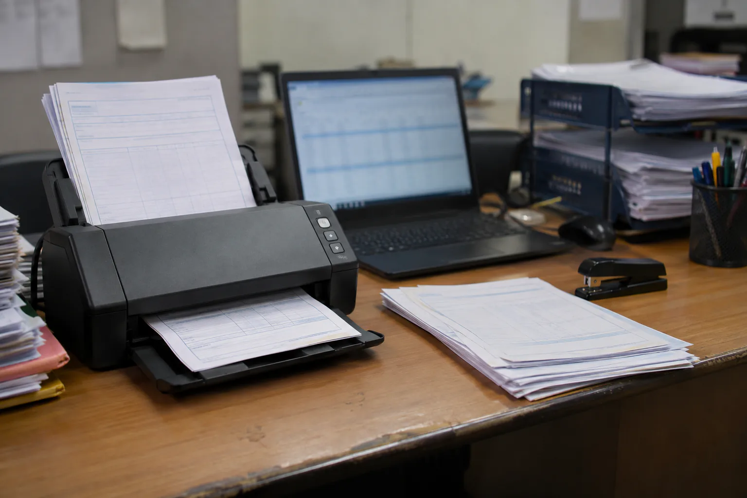 A document scanner feeding invoices beside a laptop in an accounts office